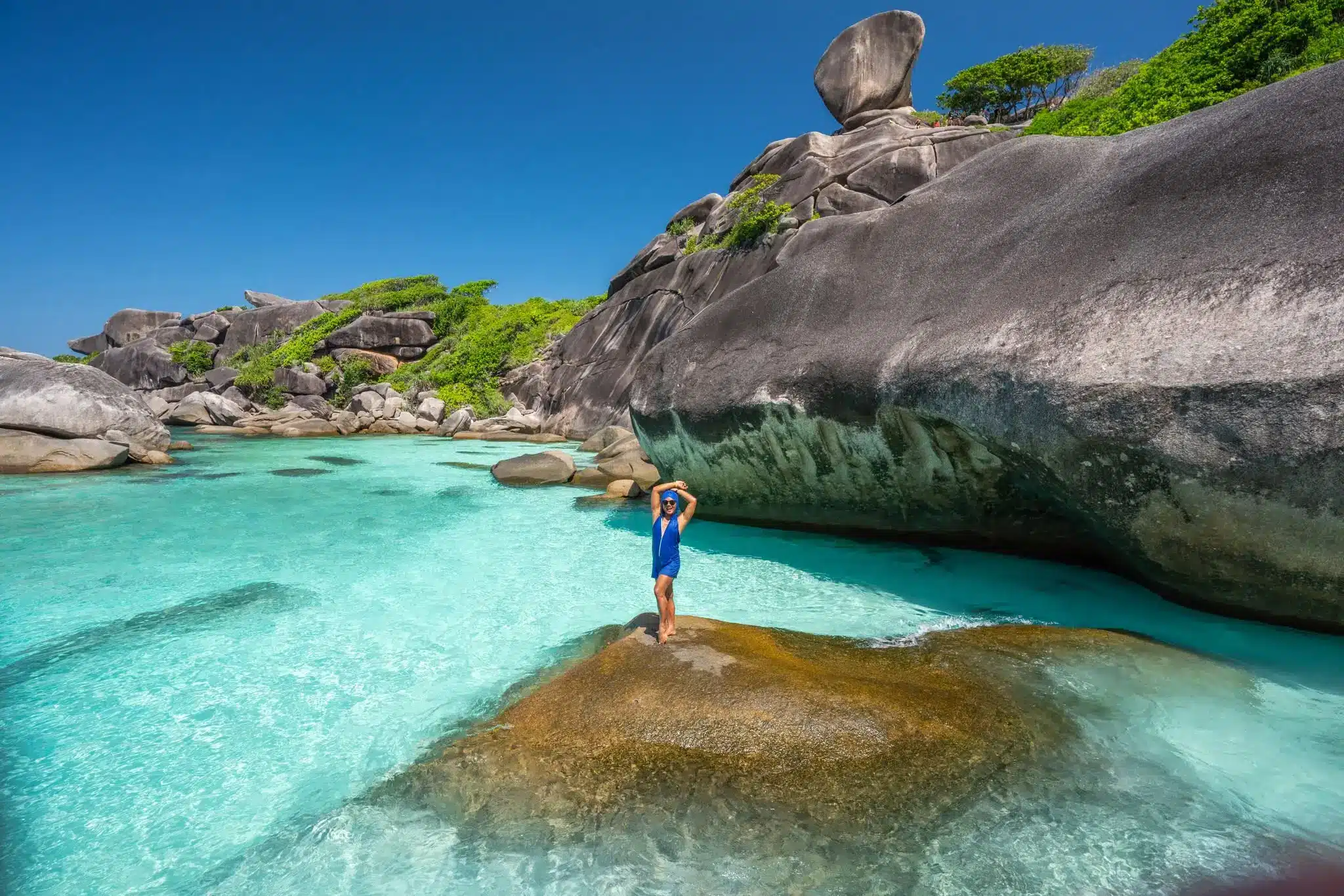 Voyageuse sur un rocher au bord de l’eau turquoise des îles Similan, sous un imposant bloc de granit