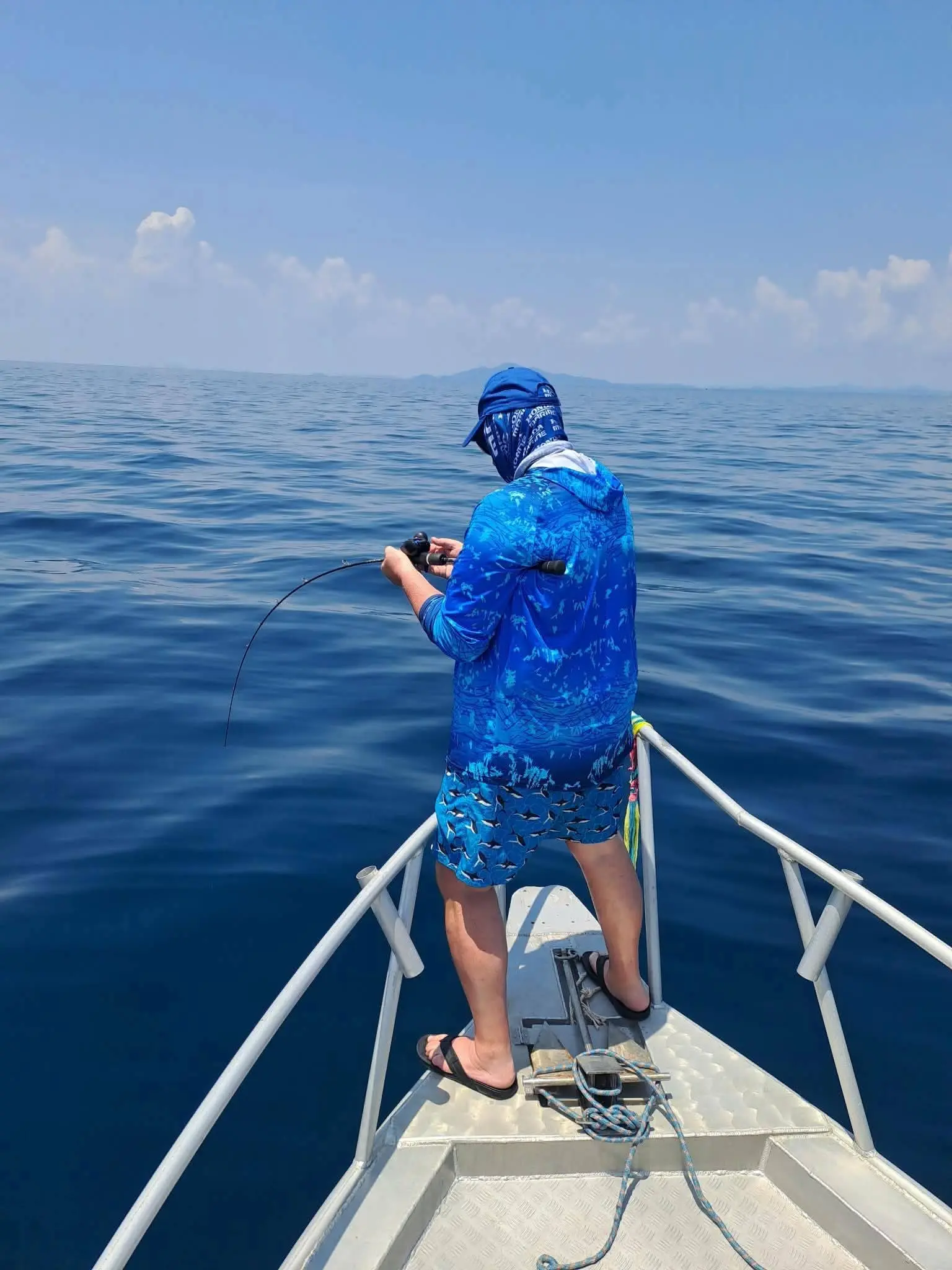 Excursion pêche : Pêcheur au jig à l’avant d’un bateau au large de Krabi, canne courbée au-dessus de la mer